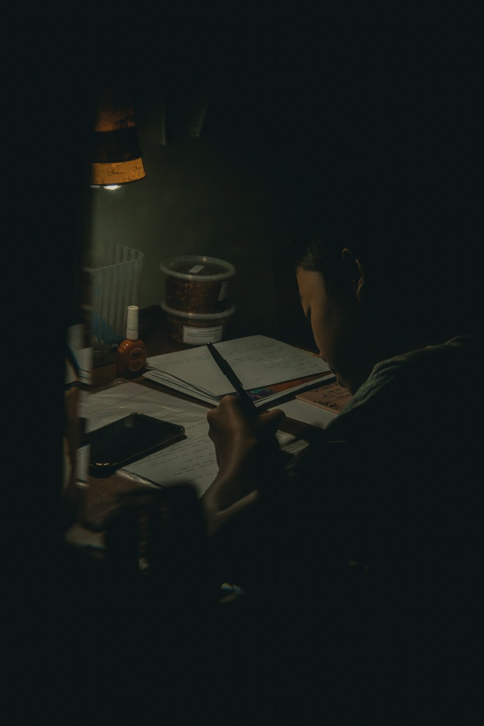 Person schreibt in ein Notizbuch an einem Schreibtisch mit einer Lampe.